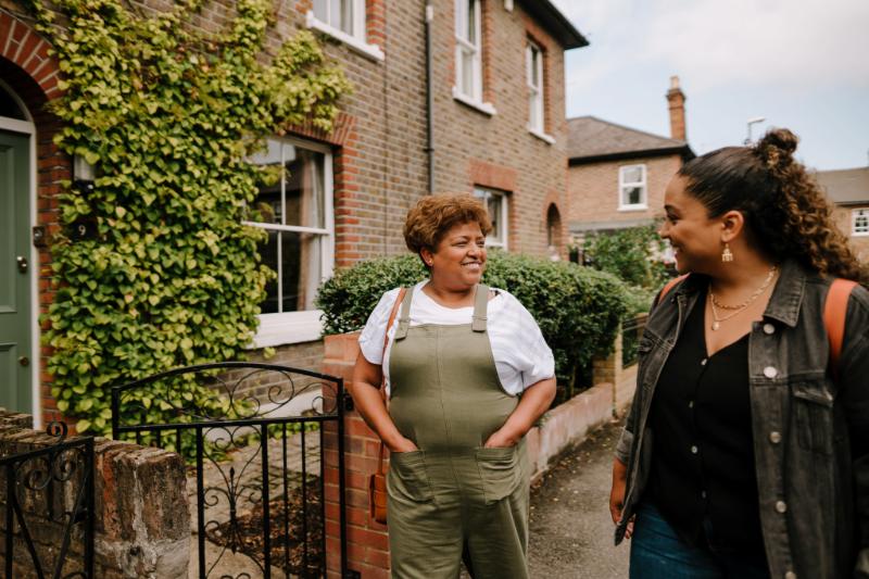 Two people standing on a residential street smiling at each other.
