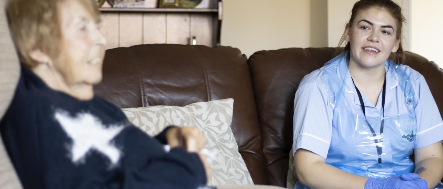 Care worker and woman talking on sofa