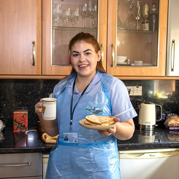 Worker standing in kitchen with a cup of tea and a sandwich